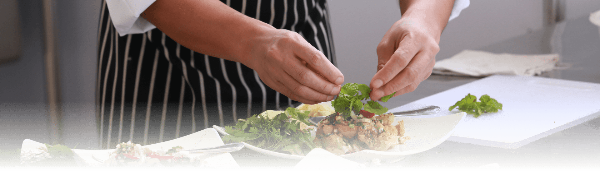 Chef in black and white striped apron plating green salads on square white places
