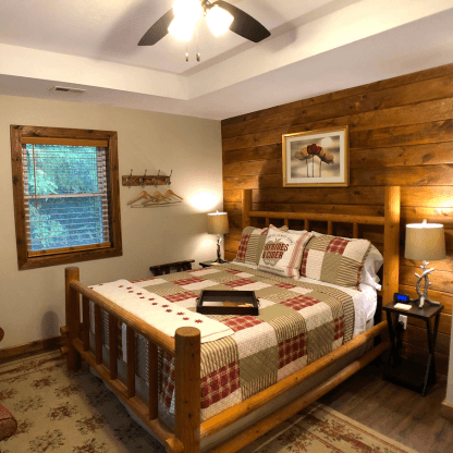 Cozy bedroom with queen log framed bed, decorative patch quilt, shiplap wall feature and bedside tables with lamps