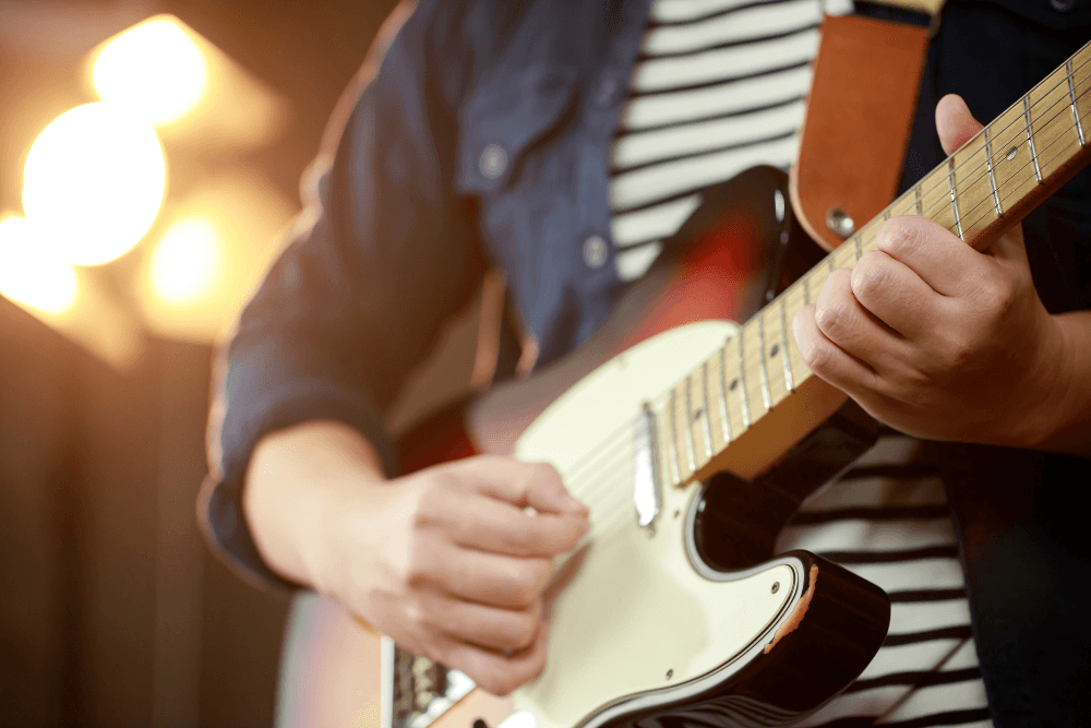 A person in a striped t-shirt and denim jacket playing an electric guitar