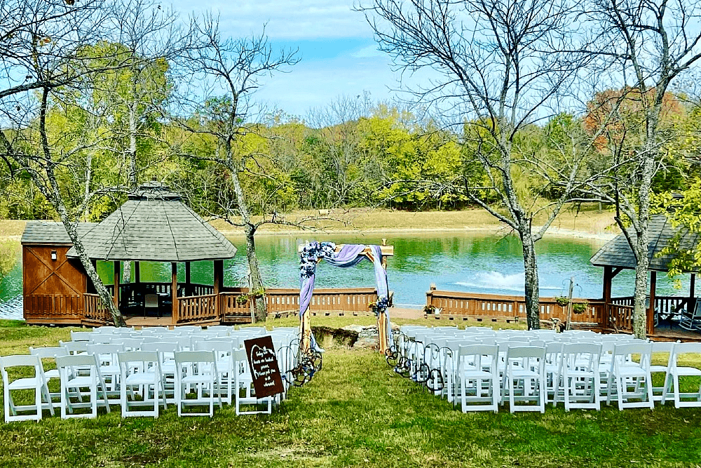 Two rows of 75 white chairs set up for a wedding in front of a pond in the fall.