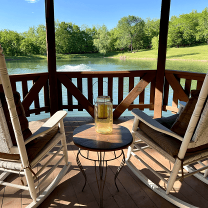Two white rocking chairs in a wooden gazebo overlooking a large pond surrounded by trees