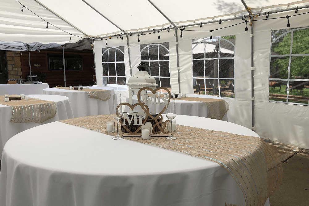 Several round tables with white linens and decor in a small tent with string light