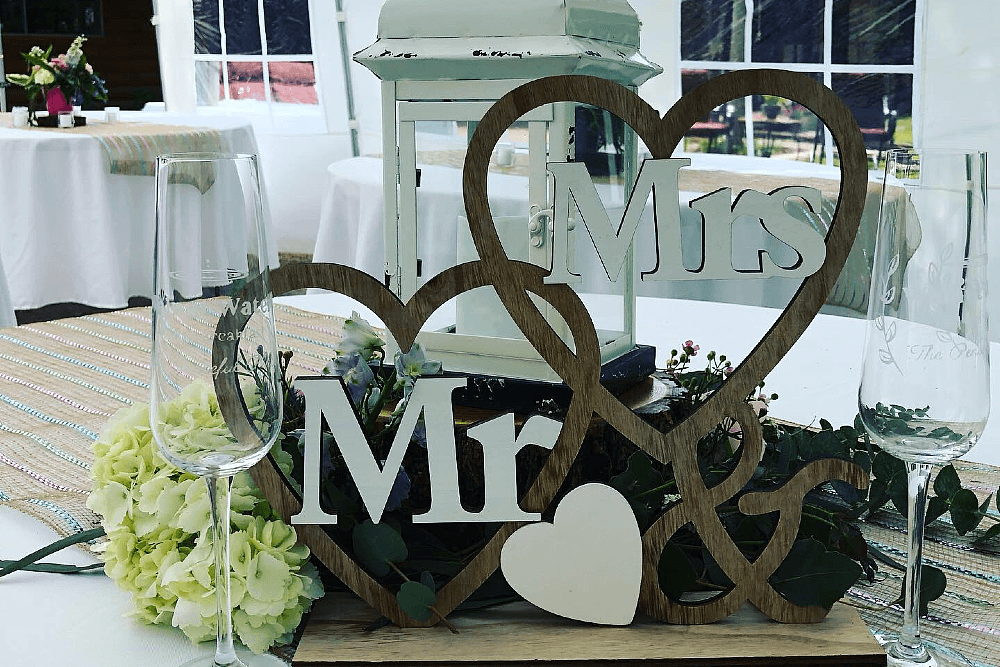 A Mr. & Mrs. sign with wood hearts on a table with greenery and flowers