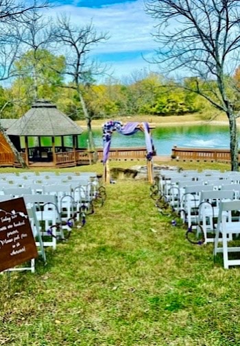 Outdoor wedding set up with white chairs and an arbor with a pond in the background