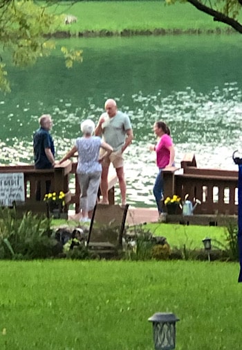 People enjoying a beverage standing on a deck by a pond