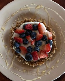 White place with round granola tart topped with yogurt, sliced strawberries and blueberries and drizzled with honey